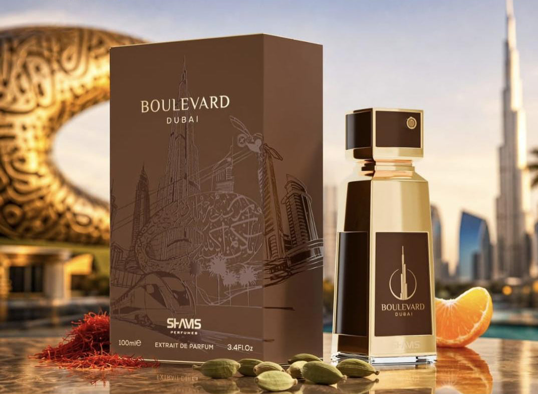 SHAMS Perfumes Extrait de Parfum 100ml bottle and its brown box packaging, styled on a reflective surface with green cardamom pods, saffron, and an orange slice against a Dubai city skyline background.